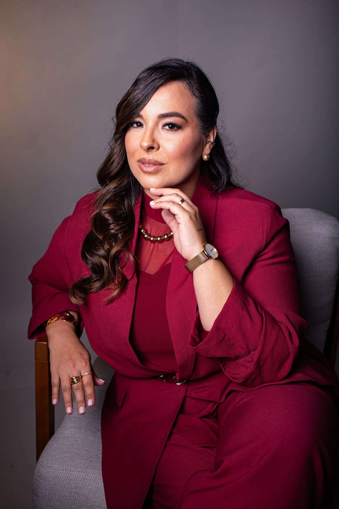 Ana Paula Silvy, de terno vinho, sentada com a mão junto ao rosto